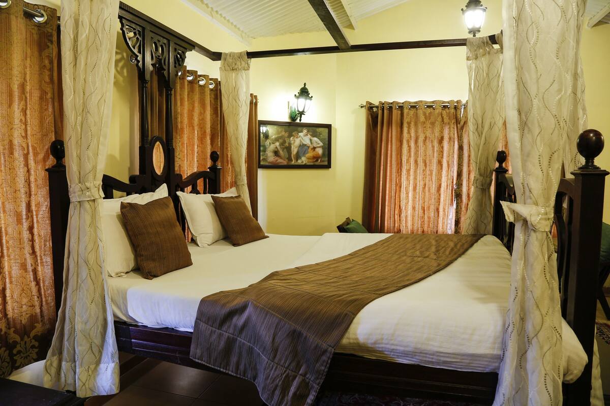 A four-poster bed with a headboard, a large painting on the wall, and curtains on the windows.