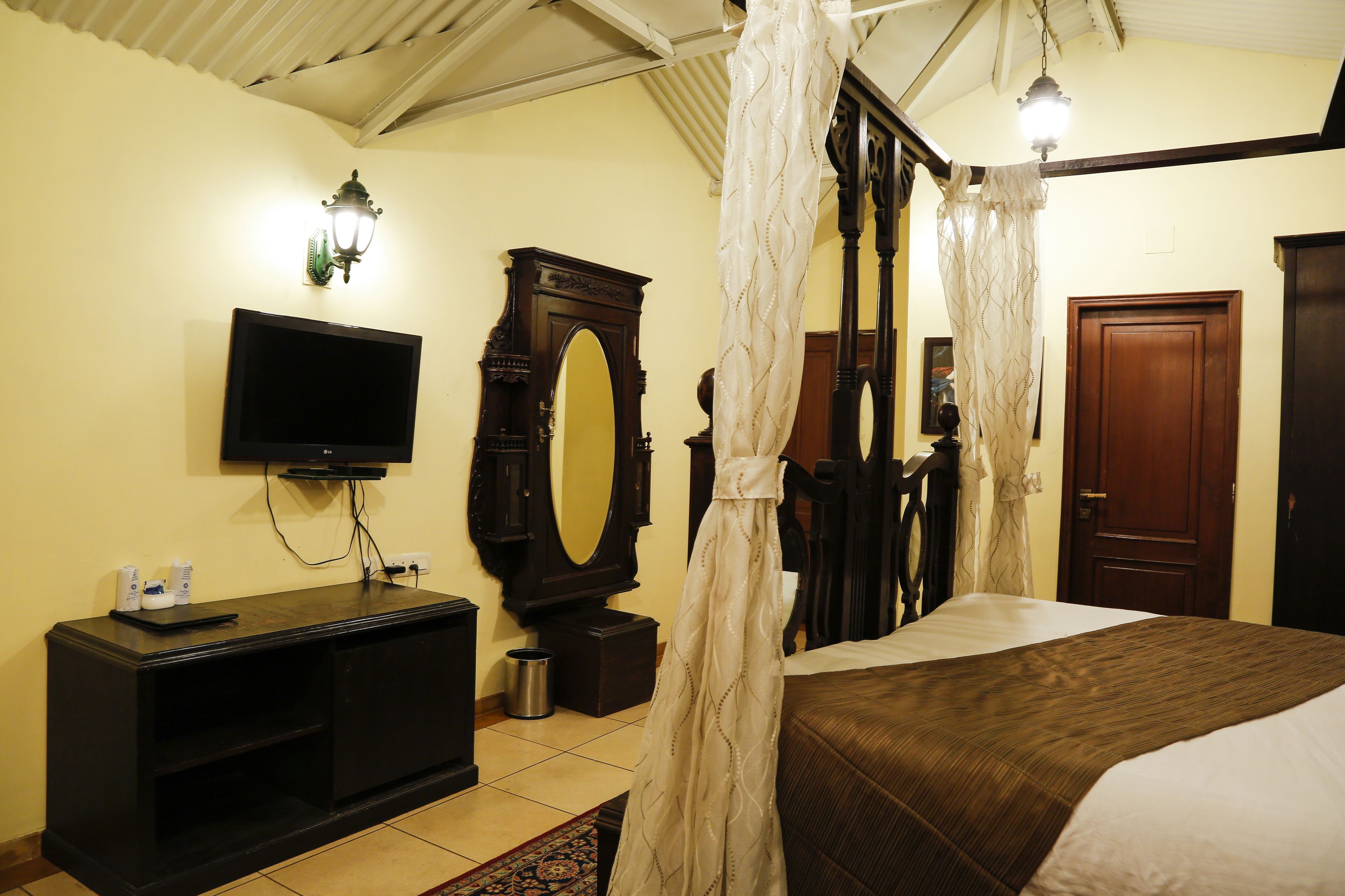 A bedroom with a bed, a television, a dresser, a mirror, and a door.
