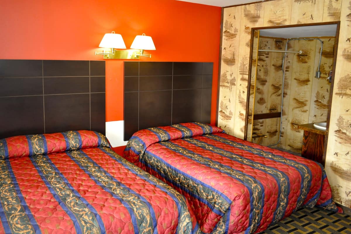 A hotel room with two beds, a black and orange wall, and a wooden panel wall with a mirror and sink.