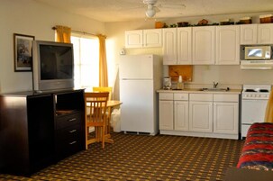 Una habitación compacta con kitchenette, zona de comedor con mesa y sillas, televisor y cama con cubrecama estampado.