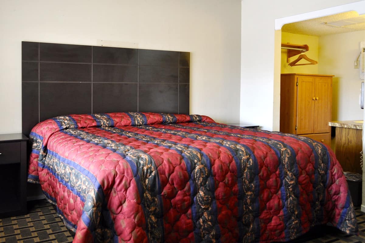 A hotel room with a large bed, a wooden wardrobe, a small bedside table, and a door leading to another room.