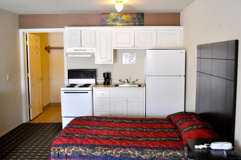 A compact hotel room with a kitchenette, a bed with a patterned bedspread, and a television on a stand.