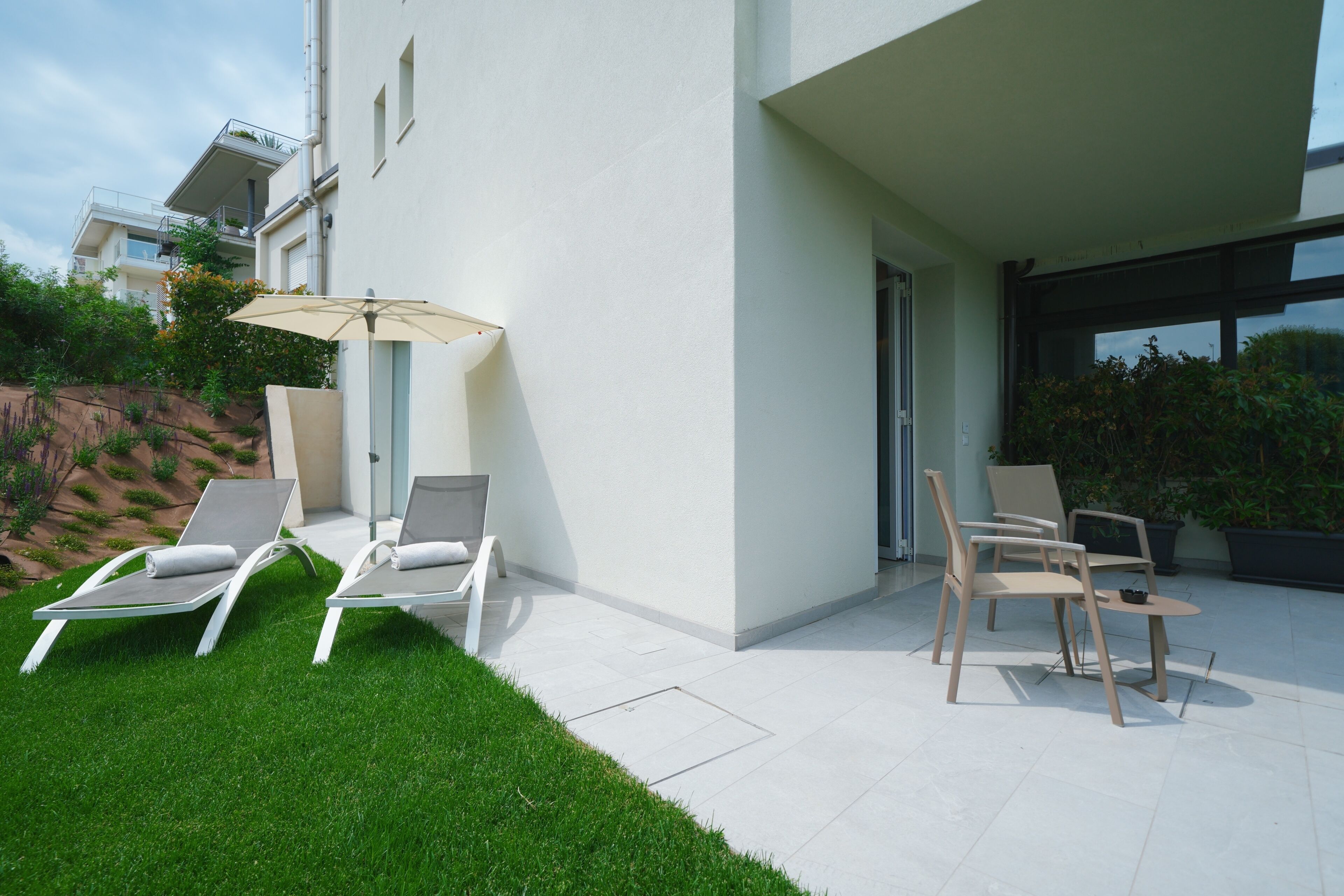 Un patio moderno all'aperto con due poltrone e un tavolo, circondato da un prato curato e piante in vaso.