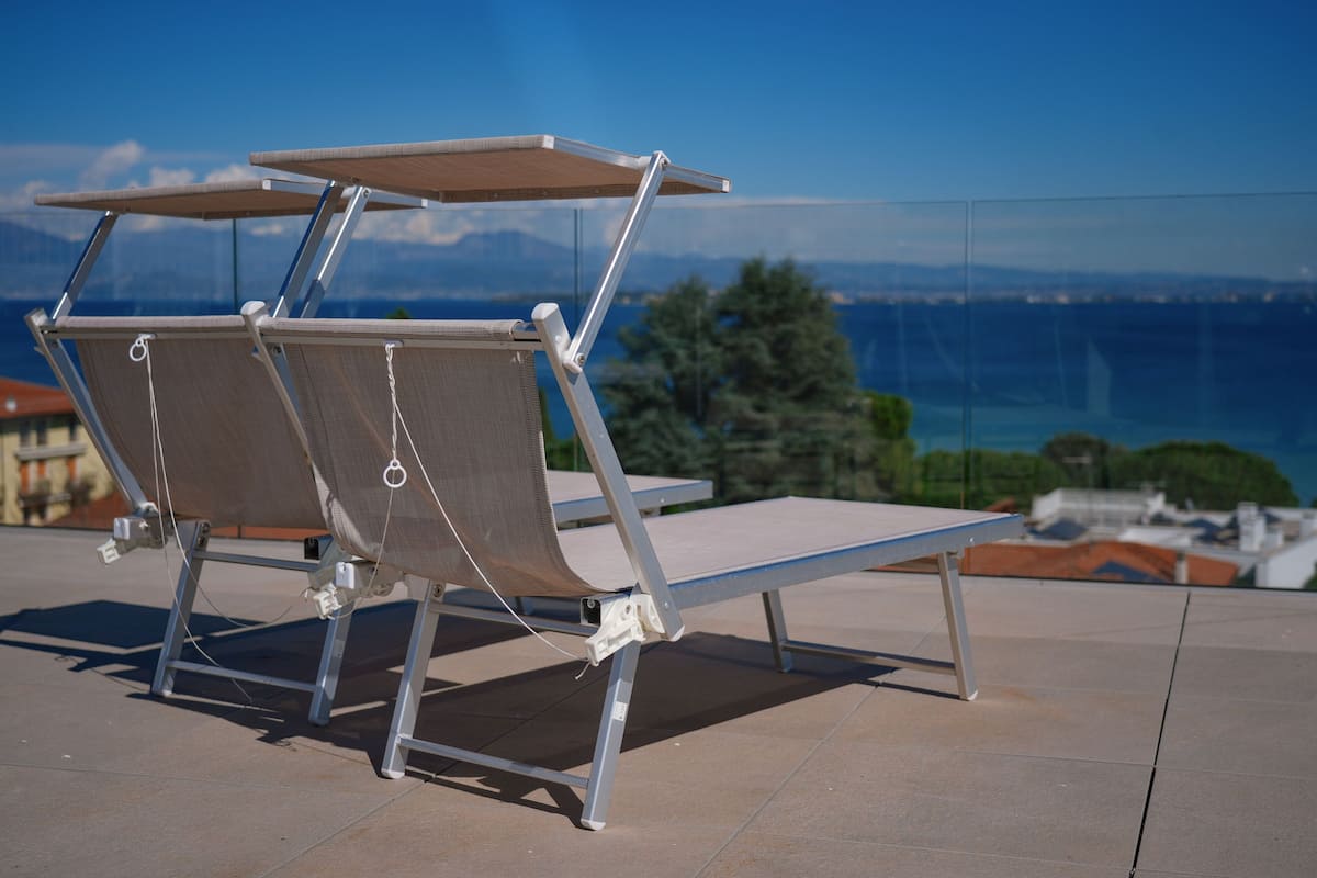 Un conjunto de sillones de exterior con estructura metálica y asientos de lona, ubicados en una terraza con vistas despejadas al mar y montañas a lo lejos.