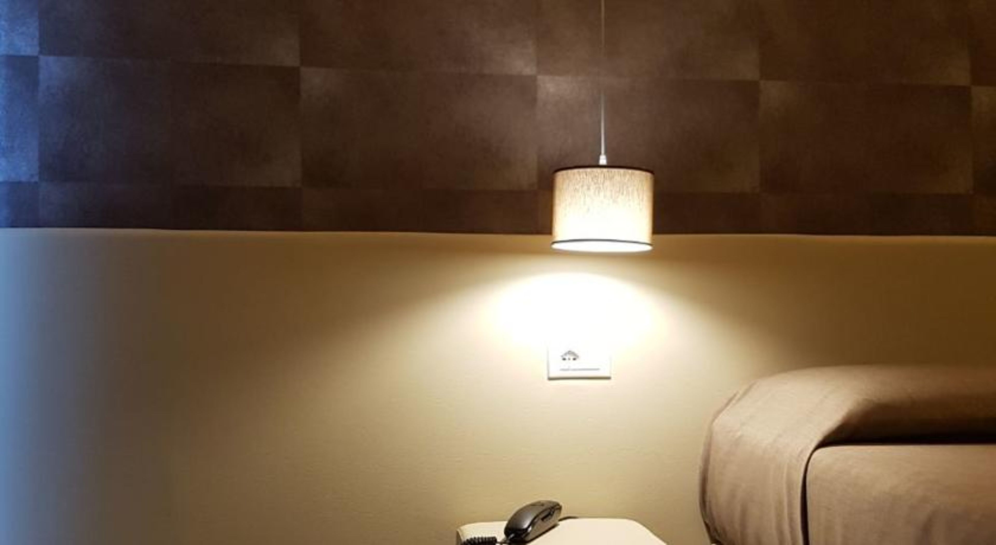 A room with a bed, a bedside table with a lamp, and a wall socket.