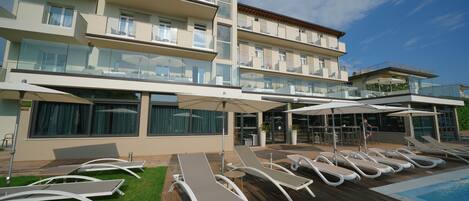 Un hotel moderno con zona de piscina, tumbonas y fachada de cristal.