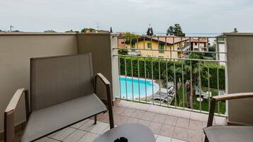 Ein Balkon mit zwei Stühlen, einem Tisch und Blick auf ein Schwimmbecken sowie Gebäude im Hintergrund.