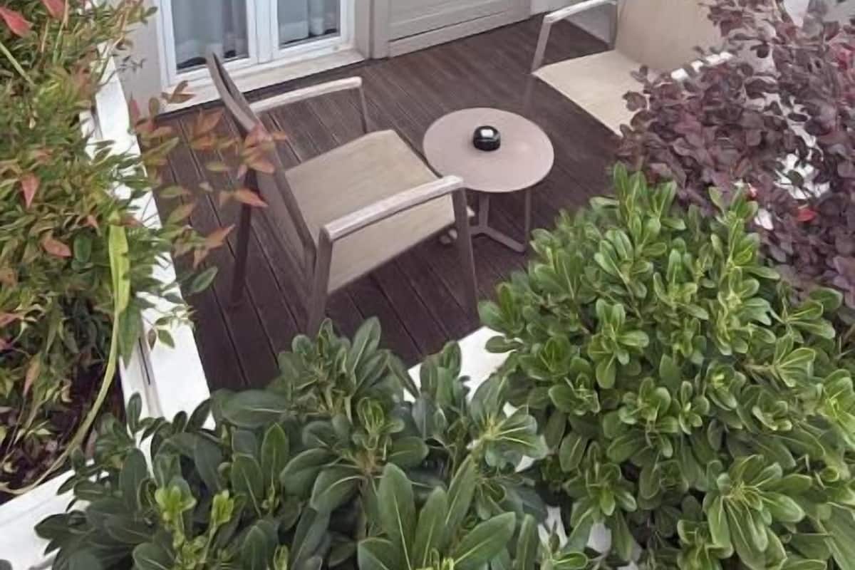 Un balcón con puerta corrediza, una mesita y sillas. Hay plantas en macetas alrededor de la zona de estar.