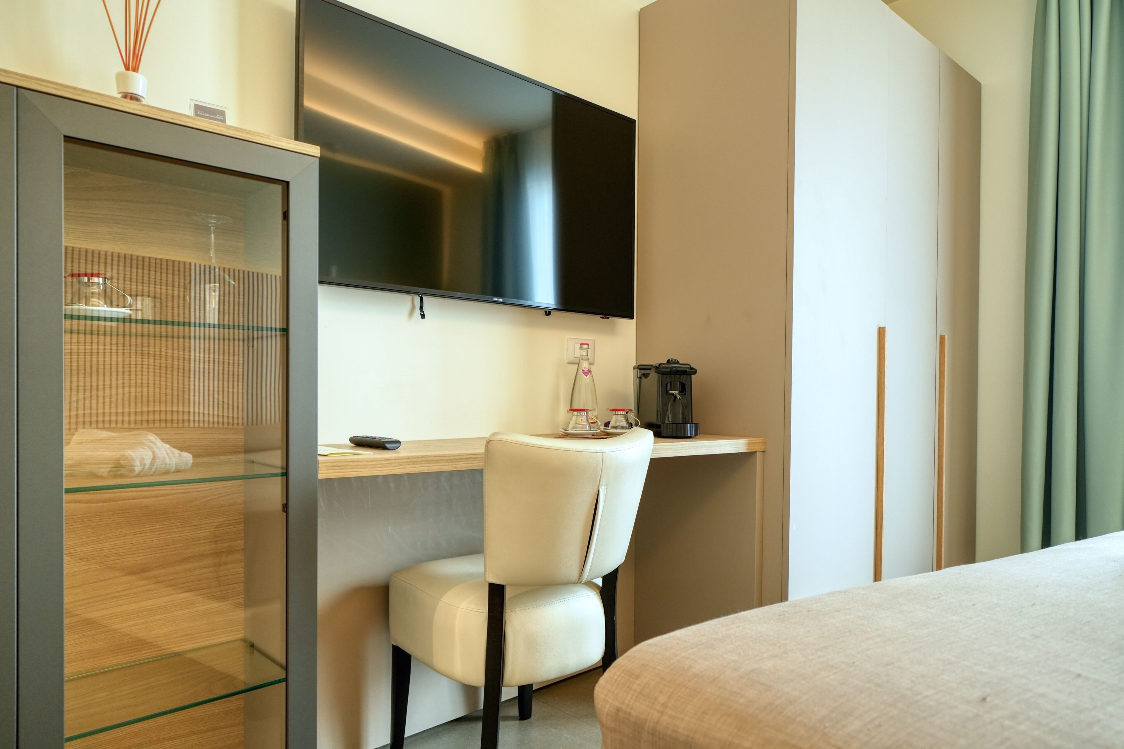 A hotel room with a bed, a desk with a chair, a TV mounted on the wall, and a minibar.