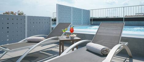 A rooftop pool area with lounge chairs and a table with drinks.