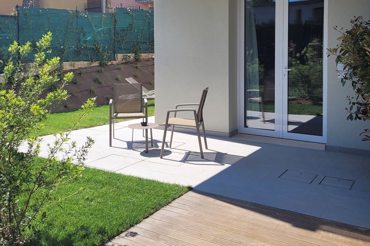 Un patio moderno con una mesa y sillas, una terraza de madera y un ventanal de vidrio que da a un jardín.