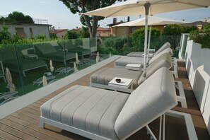 Een moderne buitenlounge met comfortabele zittingen en parasols, omgeven door glazen balustrades en een houten terras.