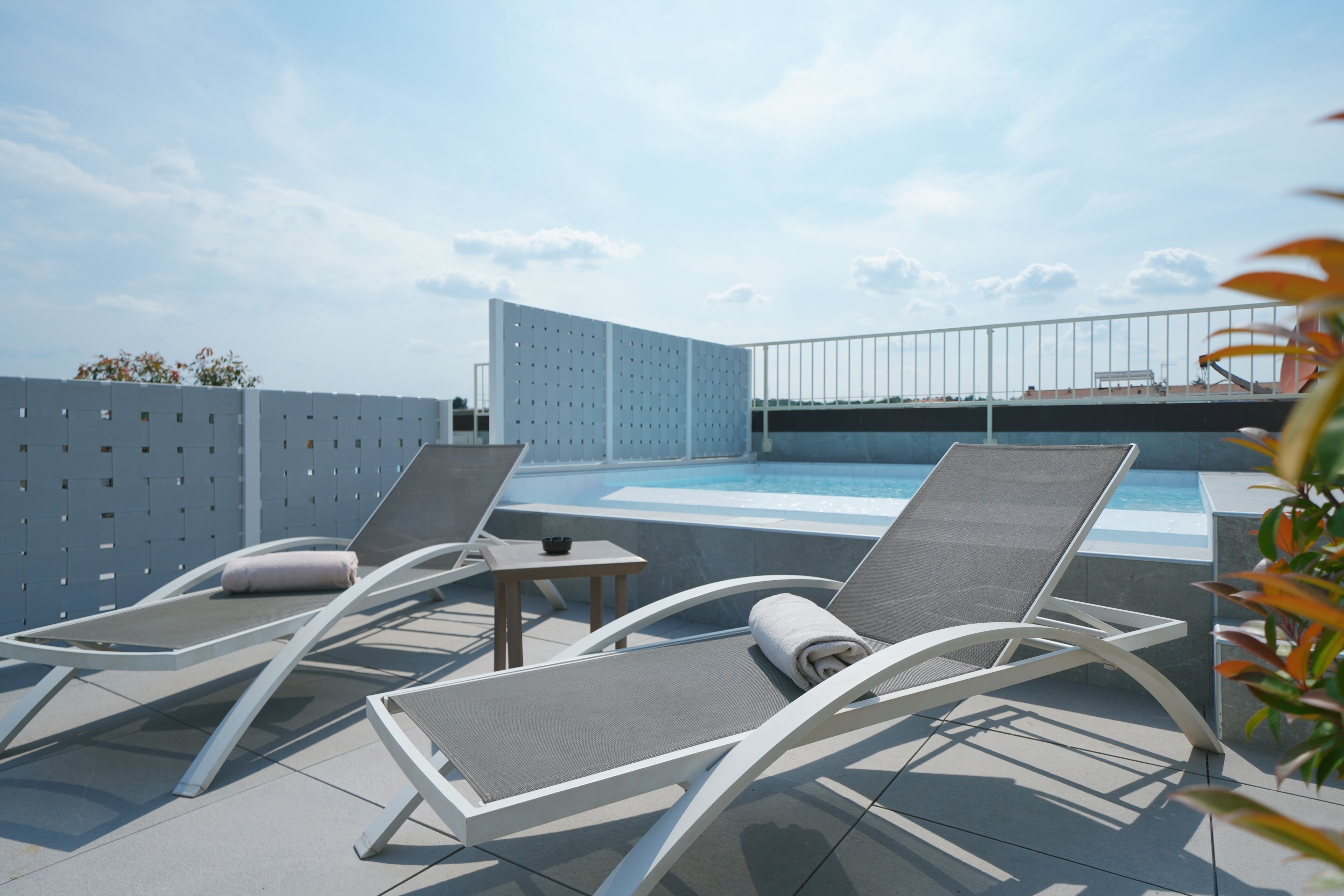 Un espace piscine aménagé sur le toit, avec deux chaises longues, une petite table et une vue sur le panorama urbain.