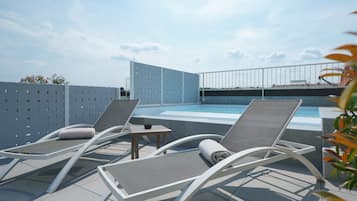 Un espace piscine aménagé sur le toit, avec deux chaises longues, une petite table et une vue sur le panorama urbain.
