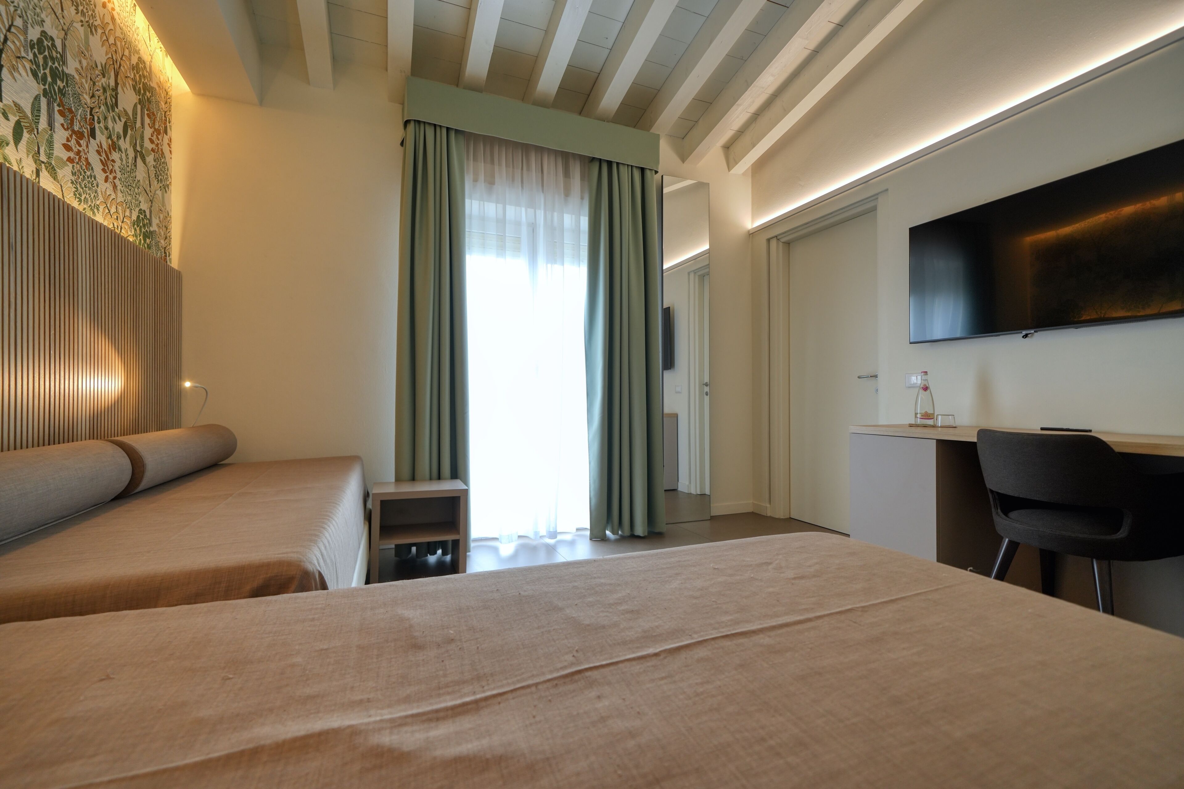Ein Hotelzimmer mit zwei Betten, einem Schreibtisch, einem Stuhl, einem Fernseher und einem Fenster mit Vorhängen.