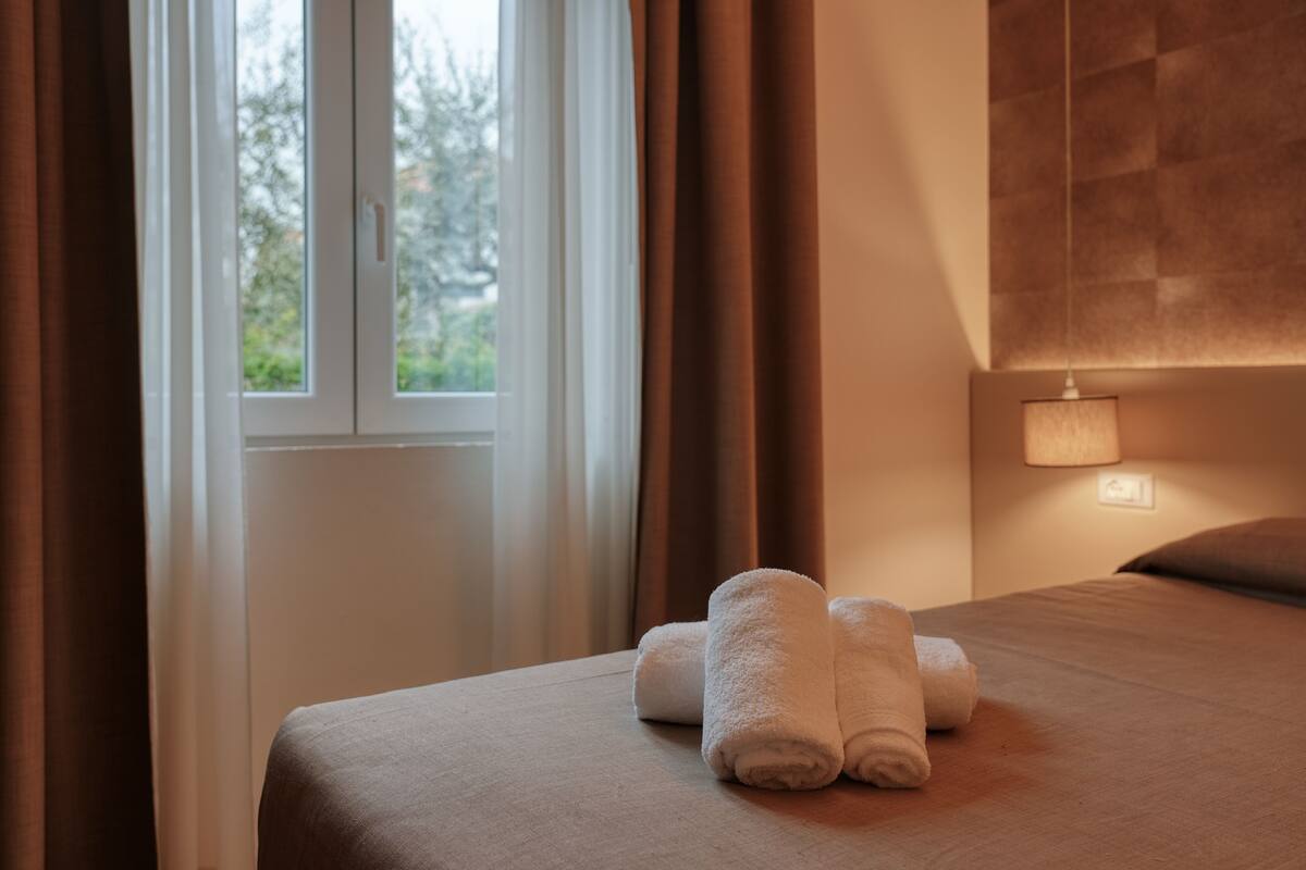 Una habitación de hotel con cama, ventana con cortinas y lámpara de pared.