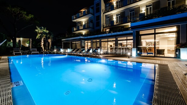 Une piscine avec des chaises longues et un bâtiment doté de nombreux balcons et de grandes fenêtres.