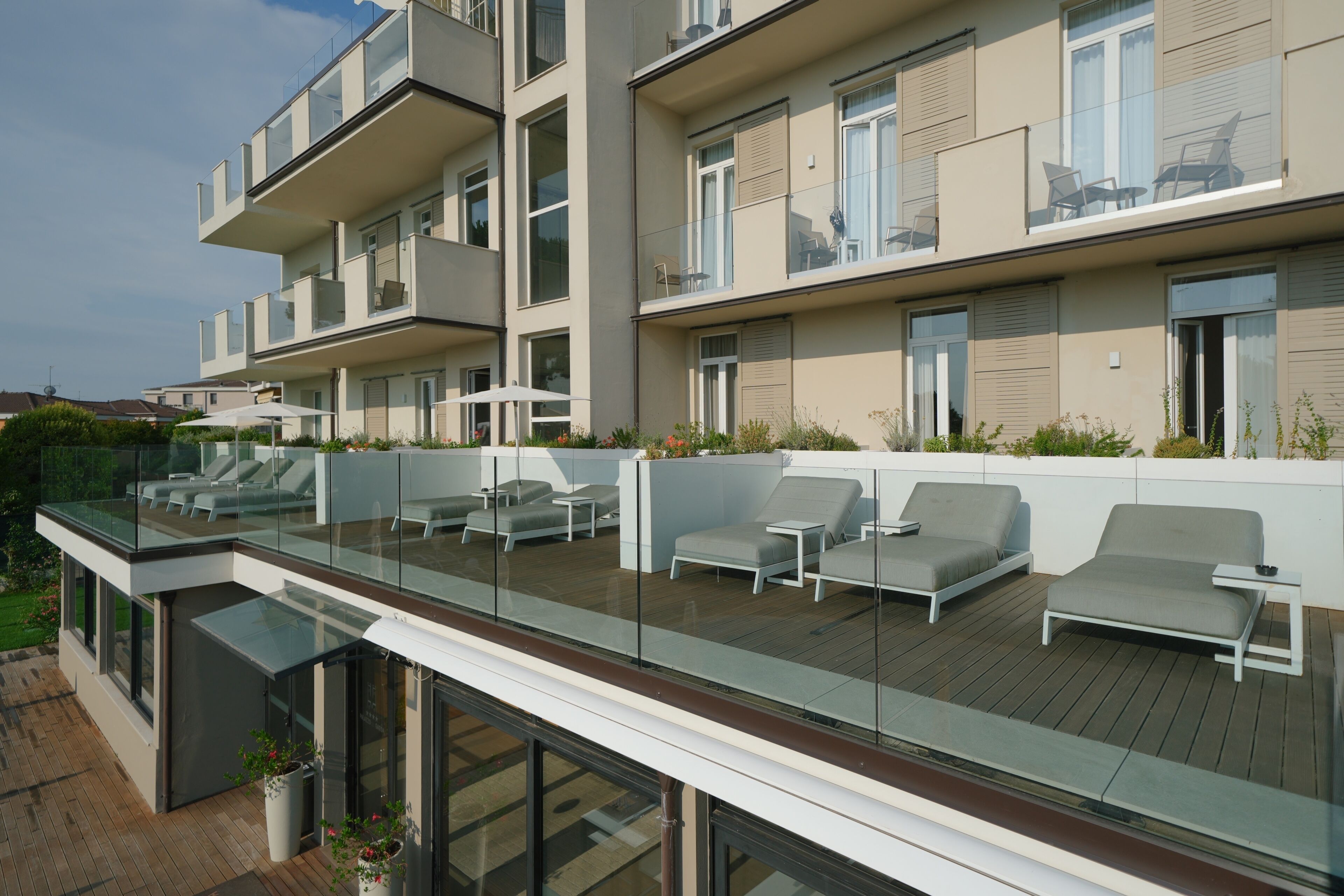 Un moderno edificio residenziale con balcone in vetro, area relax all'aperto e vista sul verde circostante.