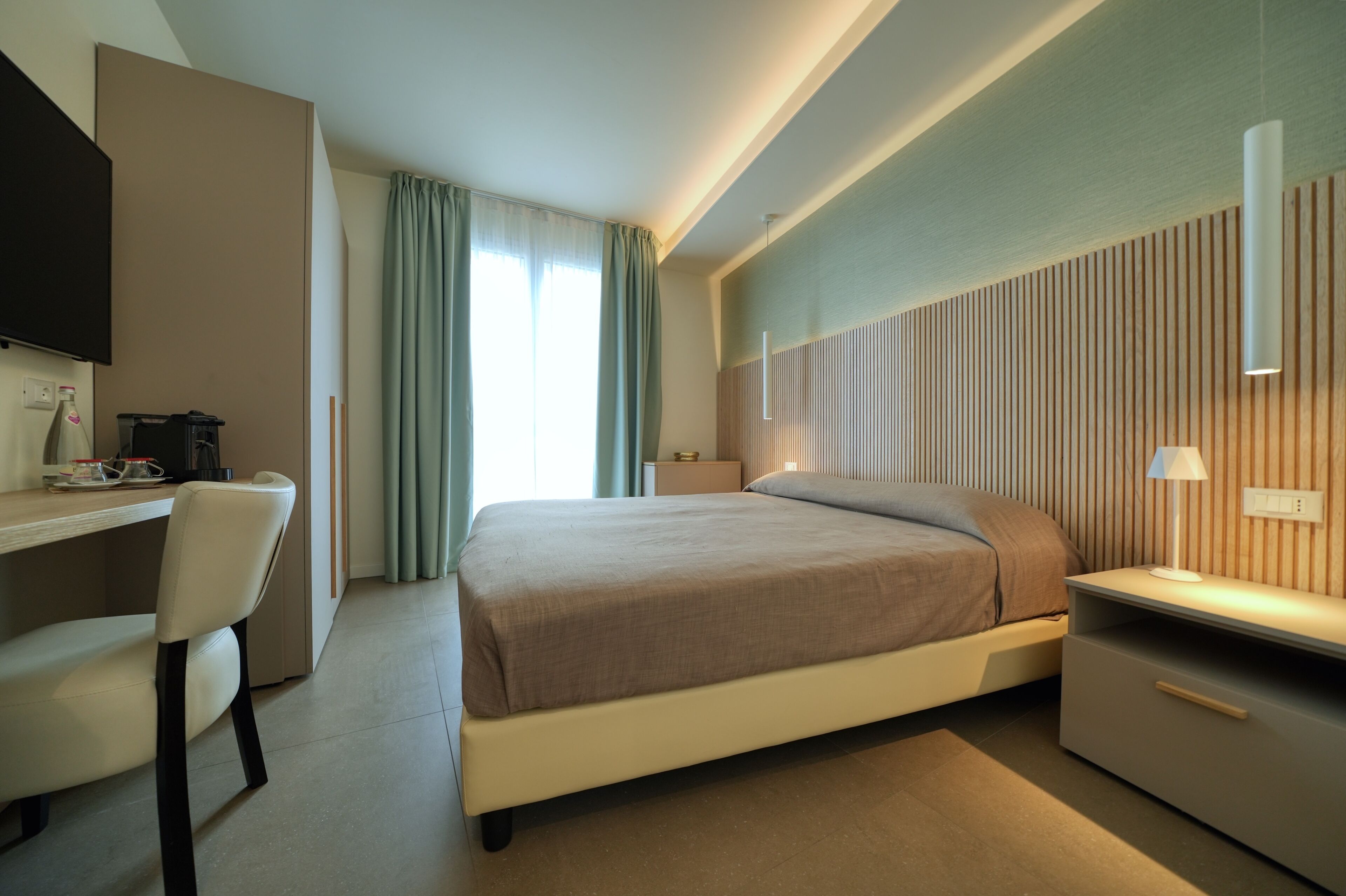 A modern hotel room with a bed, desk, chair, and a television.