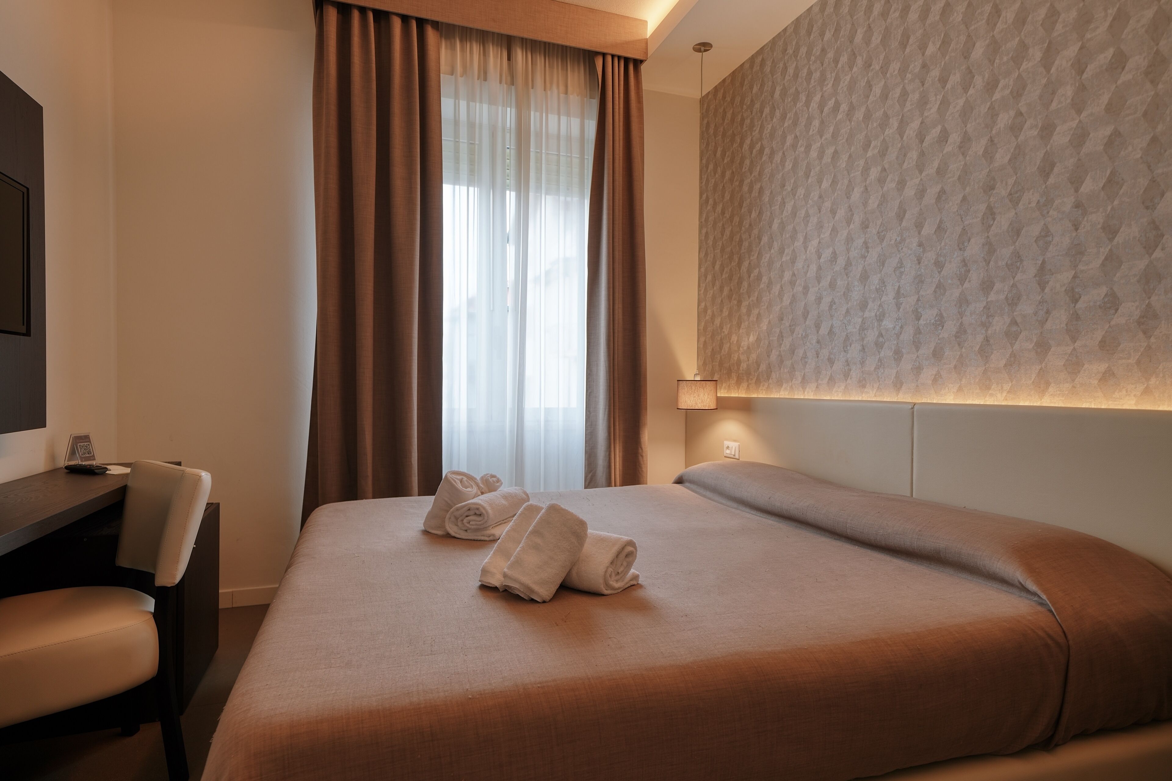A hotel room with a bed, a desk, and a chair. There are towels on the bed.
