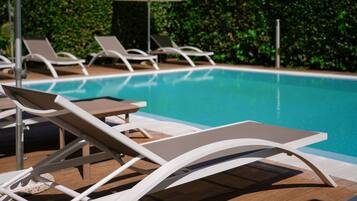 Un área junto a la piscina con sillones de descanso y sombrillas.