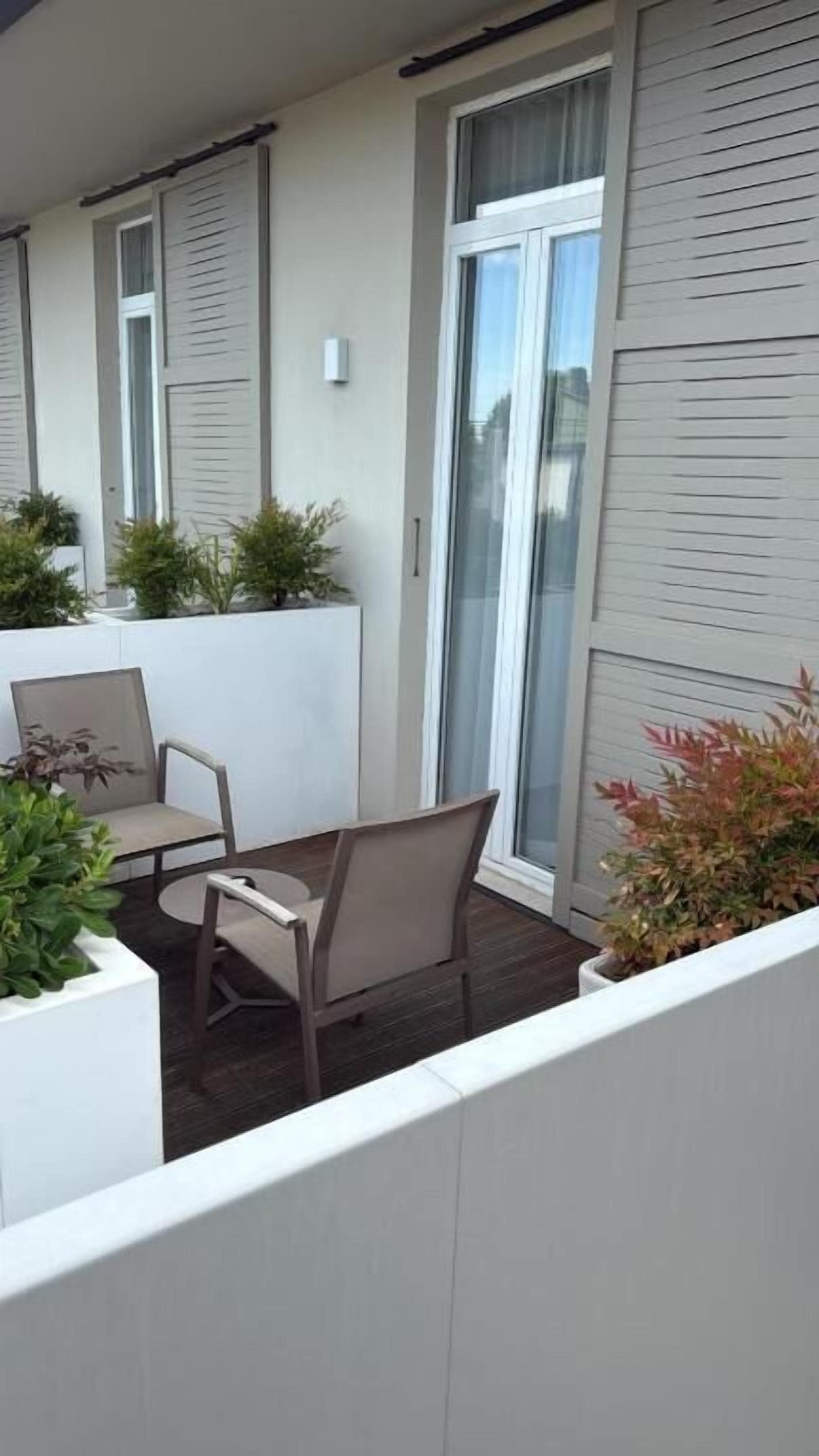 Ein Balkon mit zwei Stühlen und einem kleinen Tisch, umgeben von Blumentöpfen.