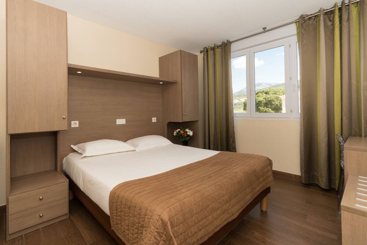 A bedroom with a bed, a nightstand, a dresser, and a window with curtains.