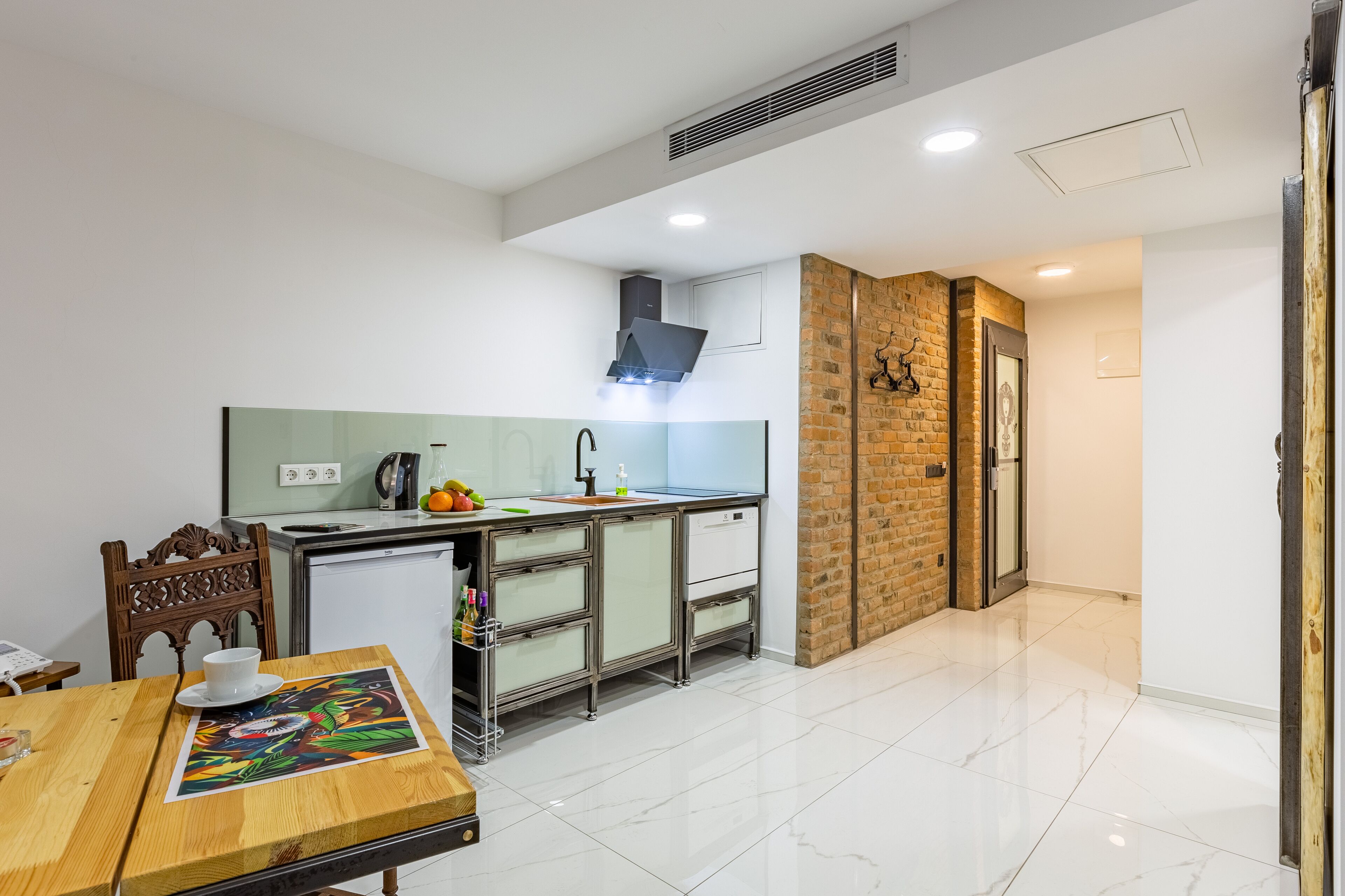 A modern kitchen with a wooden dining table, a sink, and a small refrigerator.