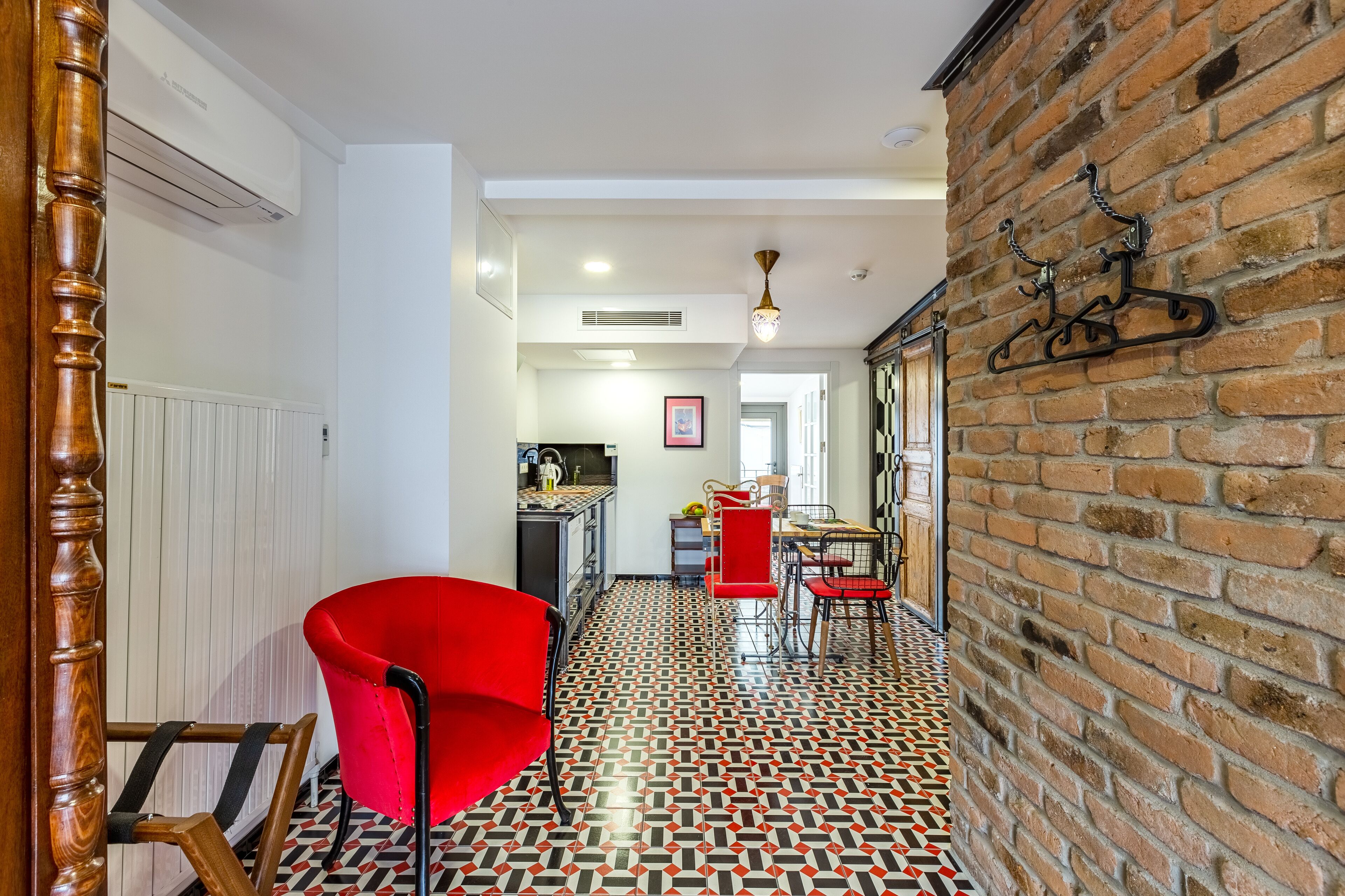 Un couloir avec une chaise rouge, un coin cuisine et un mur en briques.