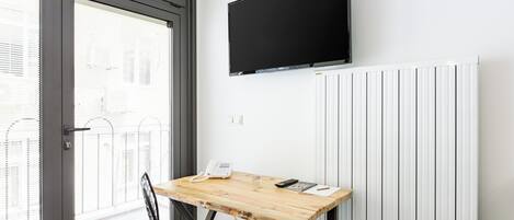 Una habitación con un escritorio de madera, una silla, un televisor montado y un radiador.