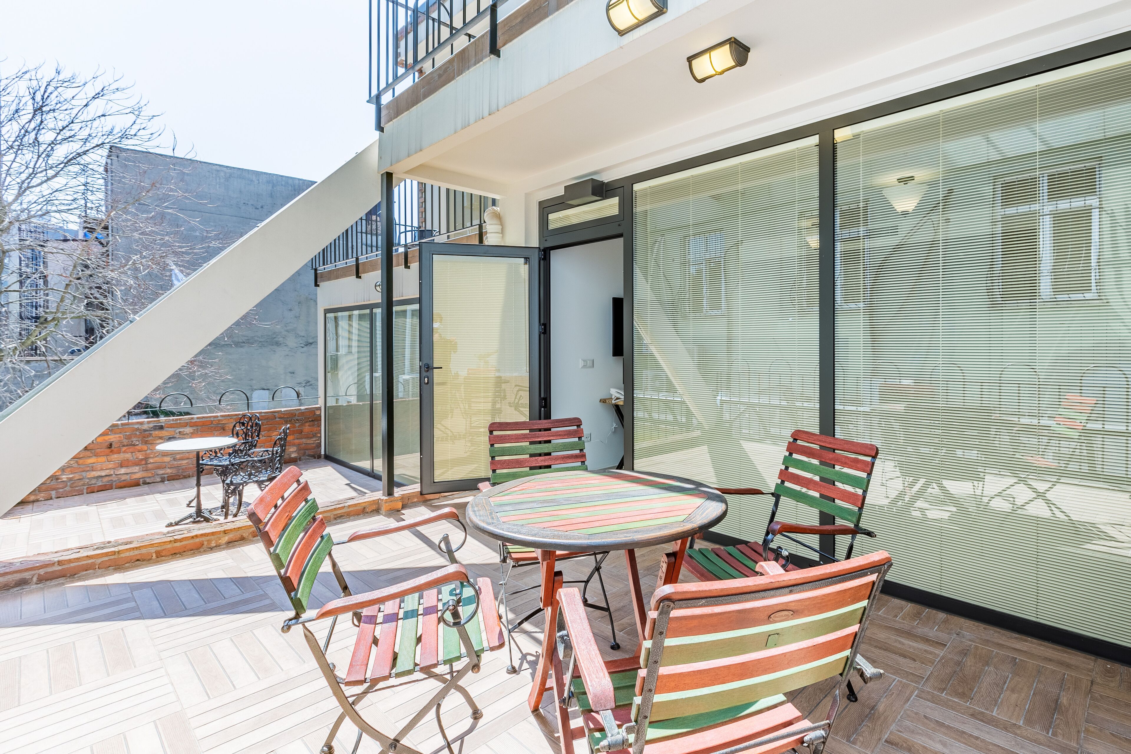 Un patio exterior moderno con puerta de cristal, sillas a rayas y una mesa redonda.