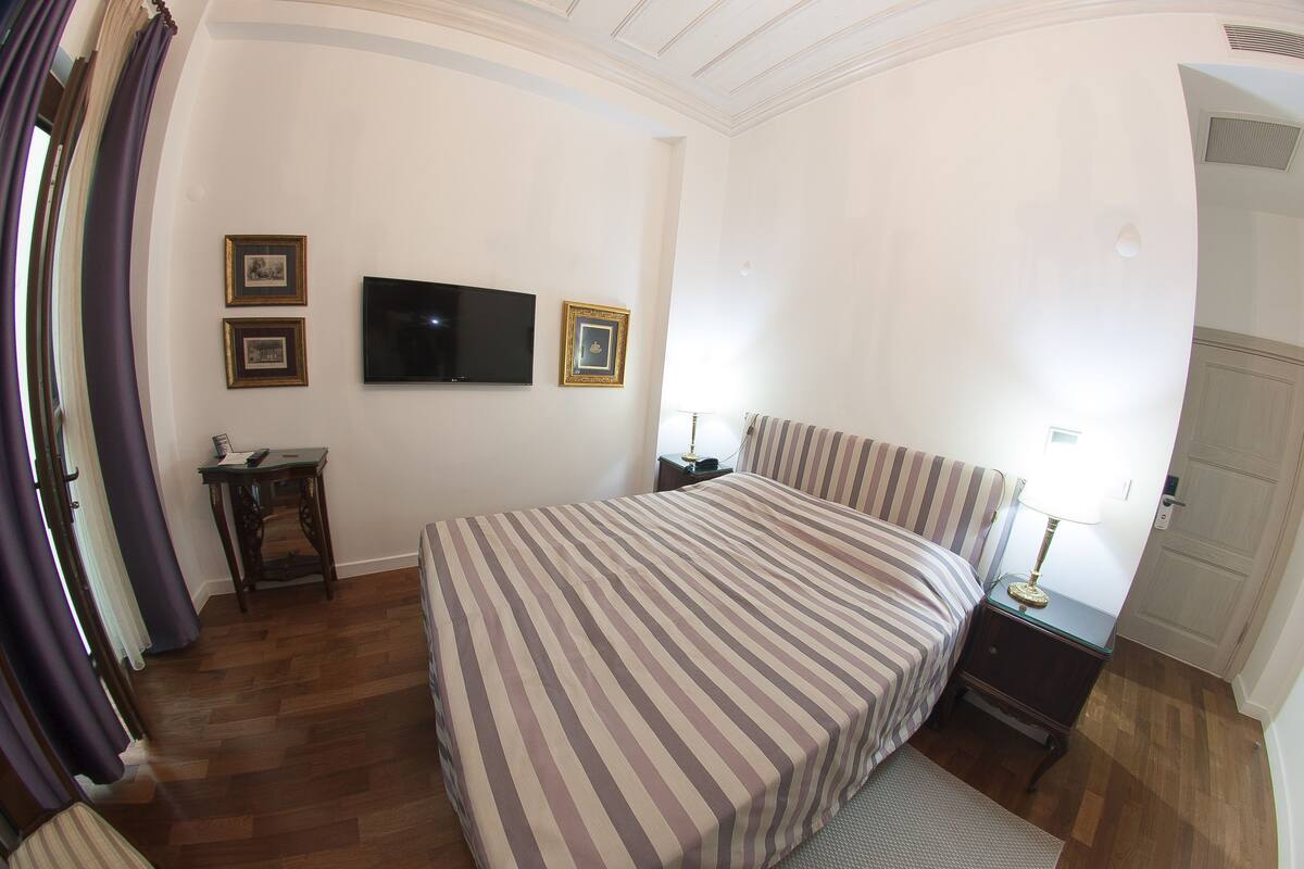 Ein Schlafzimmer mit einem großen Bett, einem an der Wand befestigten Fernseher und einem kleinen Tisch mit einer Lampe.