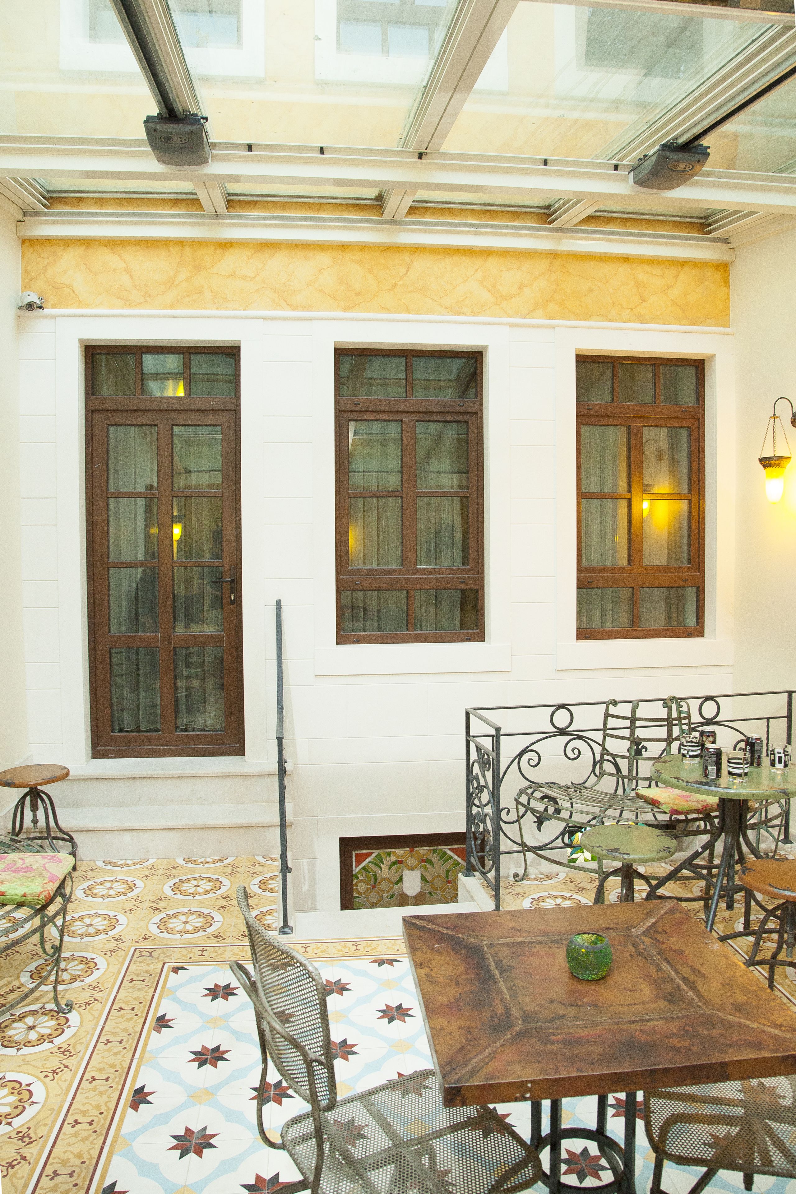 Un patio con piso de baldosas, una mesa de madera, sillas de metal y baranda de vidrio.