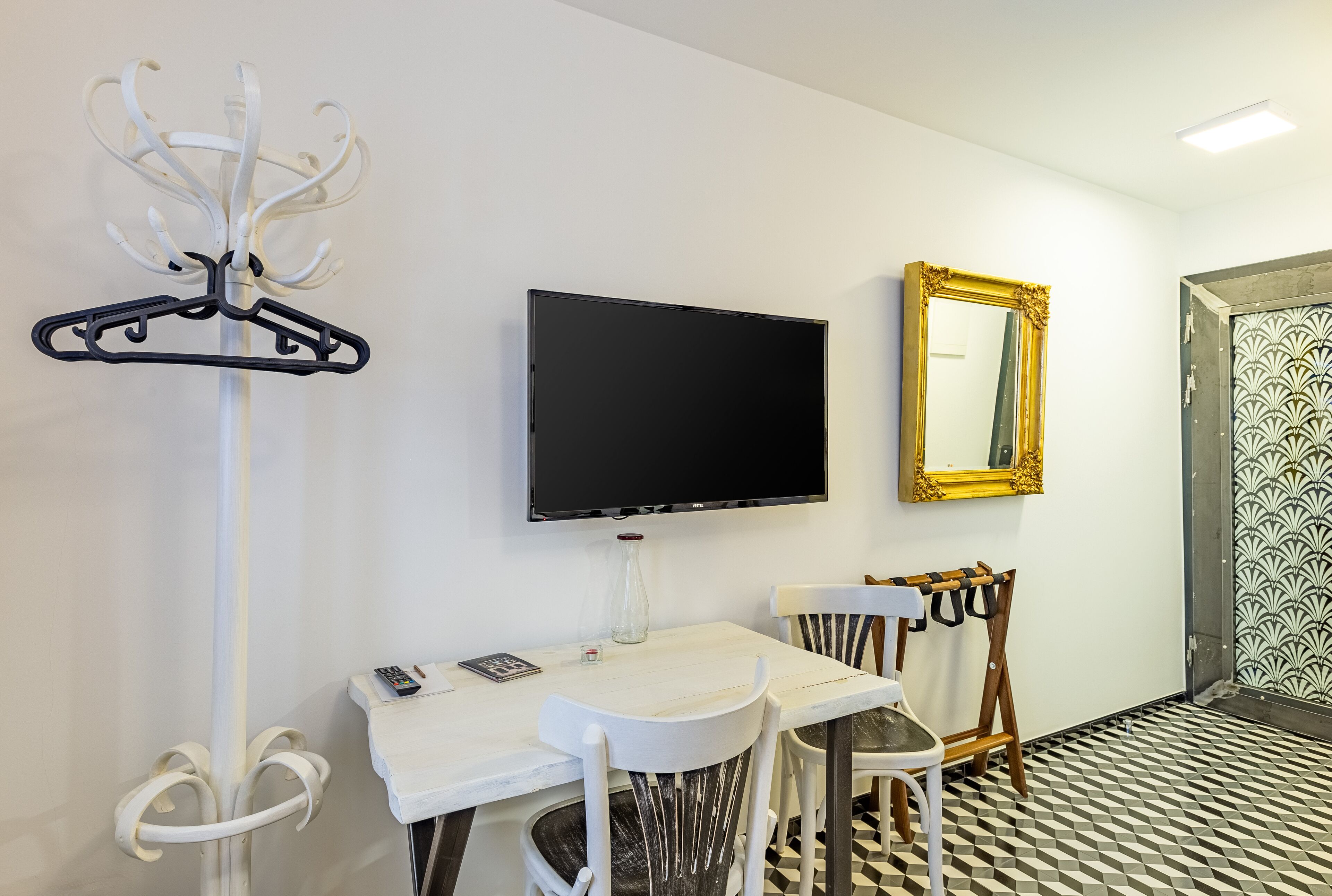 Habitación de hotel con televisión, espejo, perchero, mesa con sillas y suelo estampado.