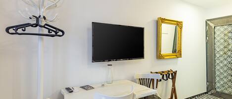 Habitación de hotel con televisión, espejo, perchero, mesa con sillas y suelo estampado.