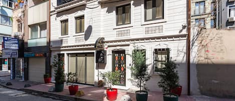 Un edificio de varios pisos con una tienda cerrada en la planta baja, plantas en macetas al frente y una antena parabólica visible.