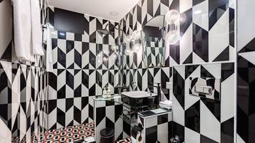 A modern bathroom with black and white geometric tiles, a glass sink, and a shower with multiple heads.