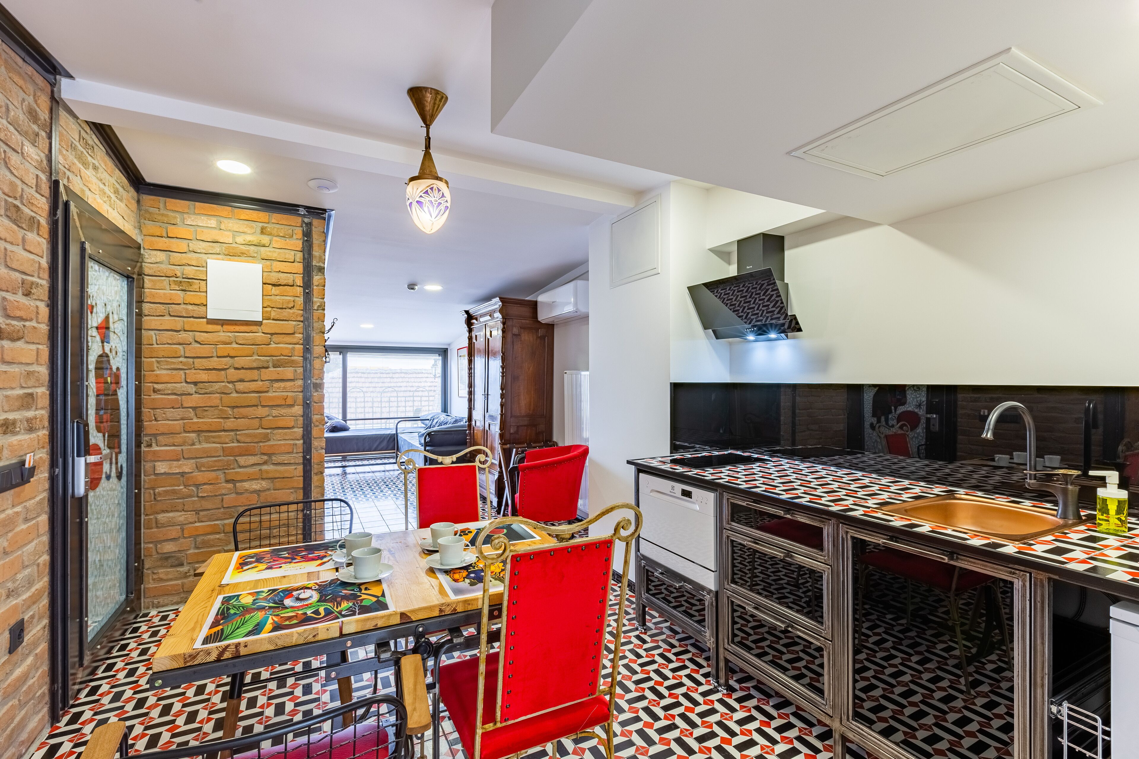 A modern kitchen with a black and white patterned floor, a wooden dining table with red chairs, and a built-in sink with a black countertop.