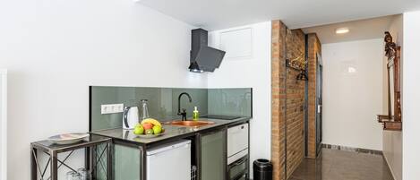 Een compacte keuken met een spoelbak, een kleine koelkast en een metalen plank.