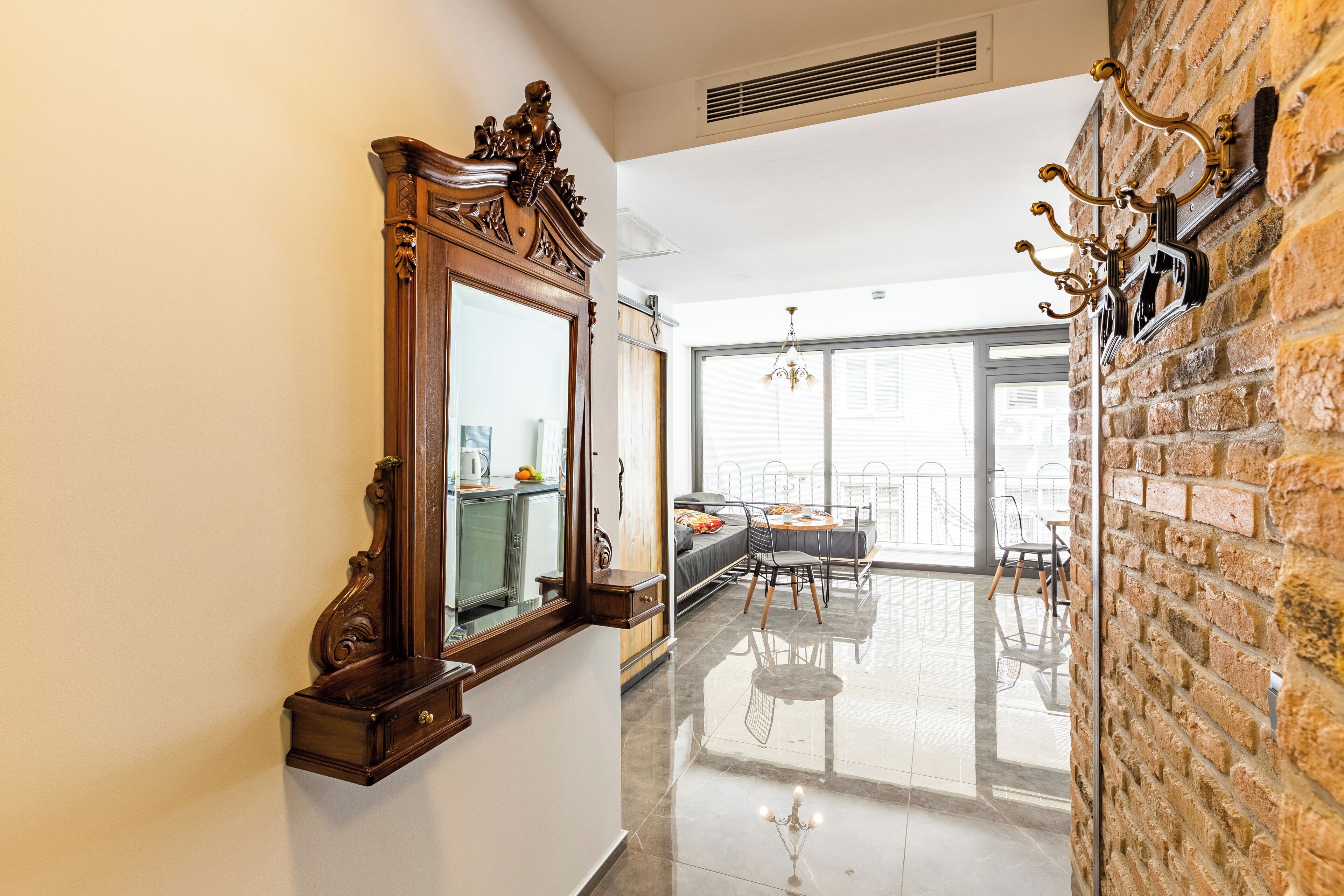 A hallway with a large mirror, a chandelier, and a brick wall.