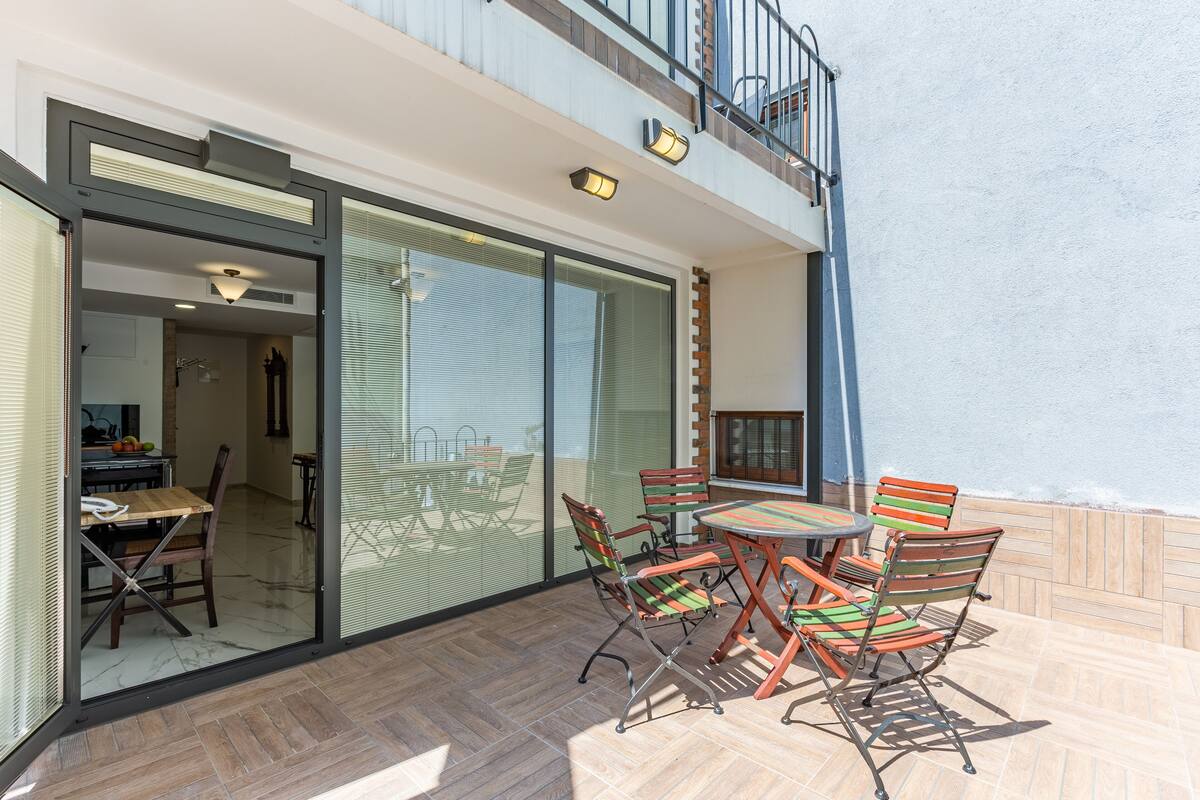 Eine Außenpatio mit Esstisch und Stühlen, eine Glastür, die zu einem Innenbereich führt, und ein Balkon mit Geländer.