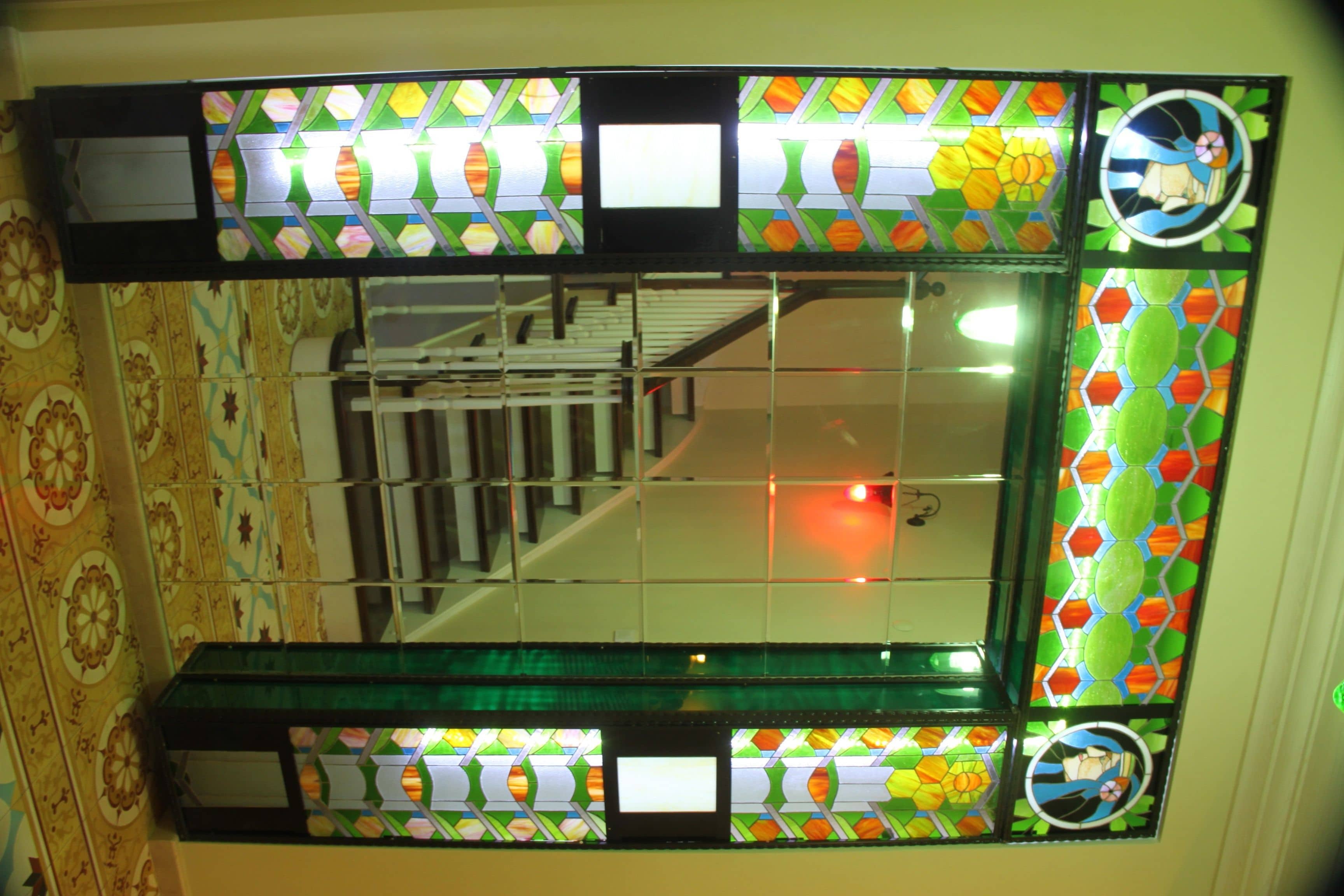 Uma janela com vitrais e padrões geométricos, refletindo uma escadaria.