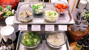 A buffet with various dishes including shrimp and cucumber salad, snap peas and cauliflower, coleslaw salad with cheese, and tomato salad.