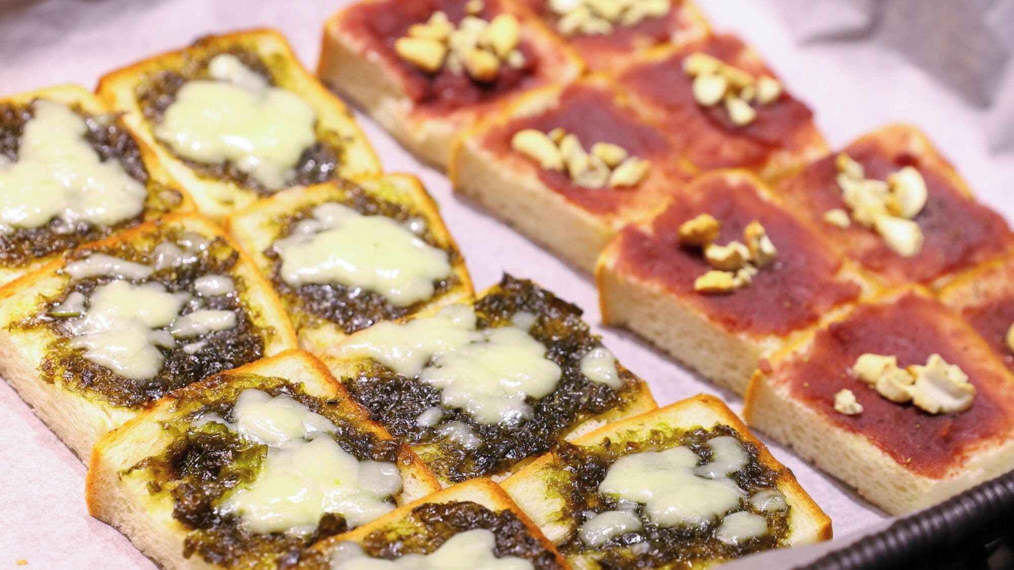 Varias porciones de bruschetta con queso derretido y un aderezo verde, posiblemente pesto, dispuestas en una bandeja.