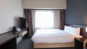 A hotel room with a large bed, a TV on a desk, a coffee maker, and a window with curtains.