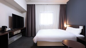 A hotel room with a bed, a TV, a desk with a coffee maker, and a bedside table.