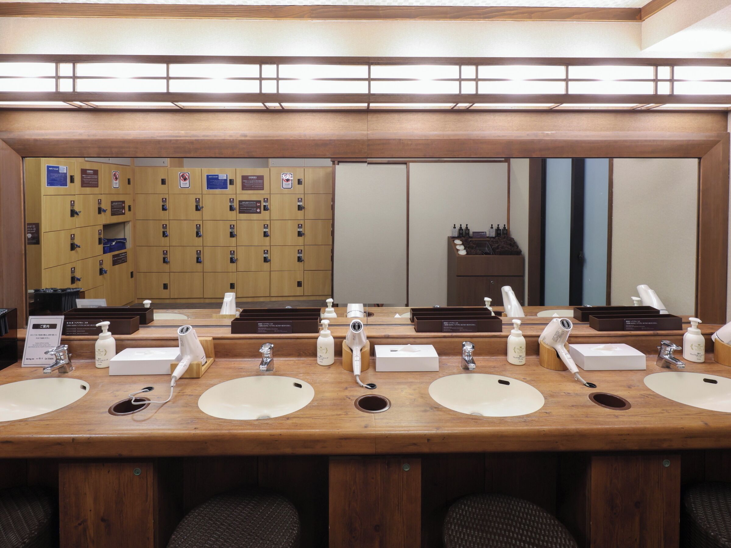 A hotel restroom with multiple sinks, mirrors, and a row of lockers in the background.