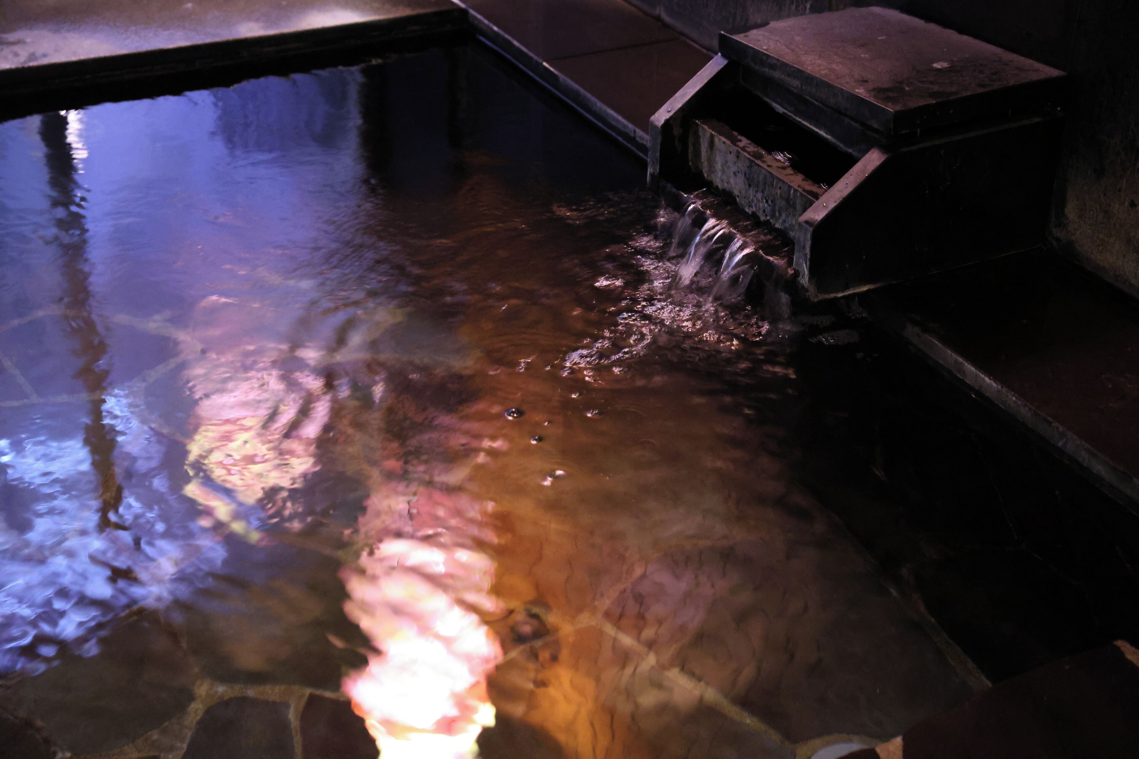 A stone pool with water flowing over a ledge, surrounded by stone walls.