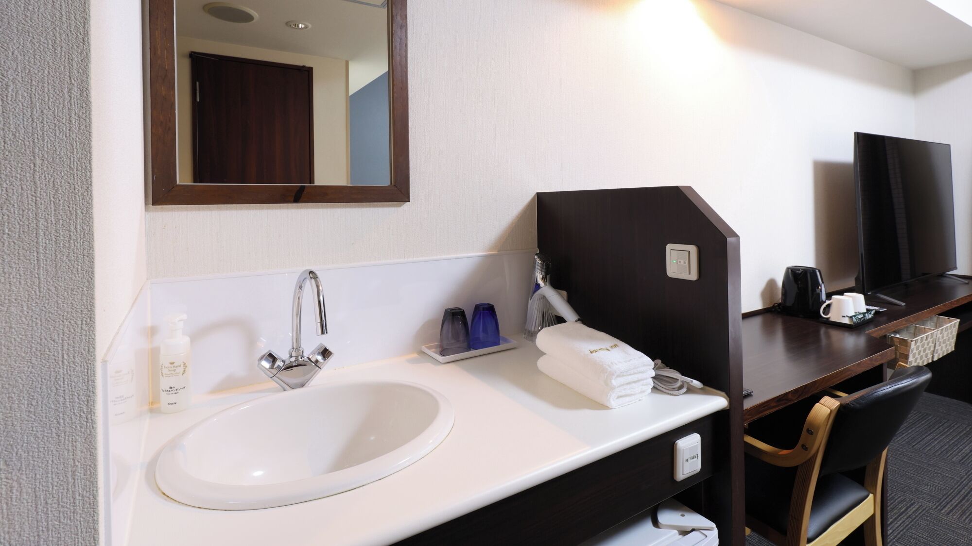Un bany d'hotel amb un lavabo, un mirall, una barra de tovalloles i una televisió.