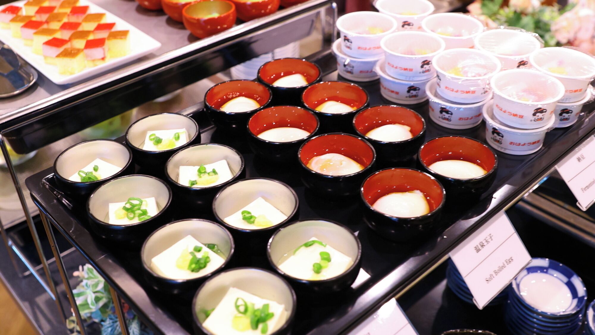 A variety of food items displayed on a counter, including bowls with a white substance and green garnish, and small cups with a red substance.